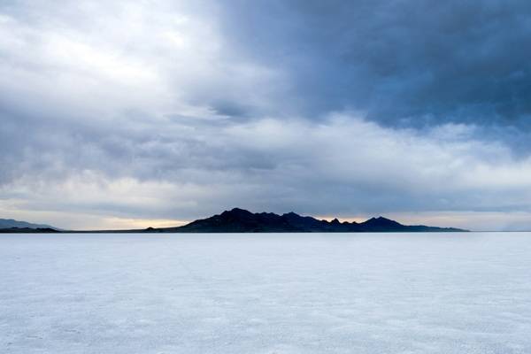 open salt flats with a small mountain behind and dramatic cloud cover