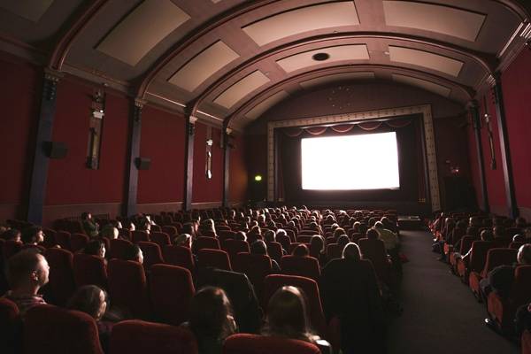 a dark movie theater with a lit screen and full of people watching