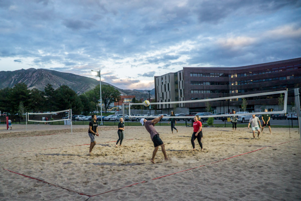 a group of students playing sand volleyball in the evening